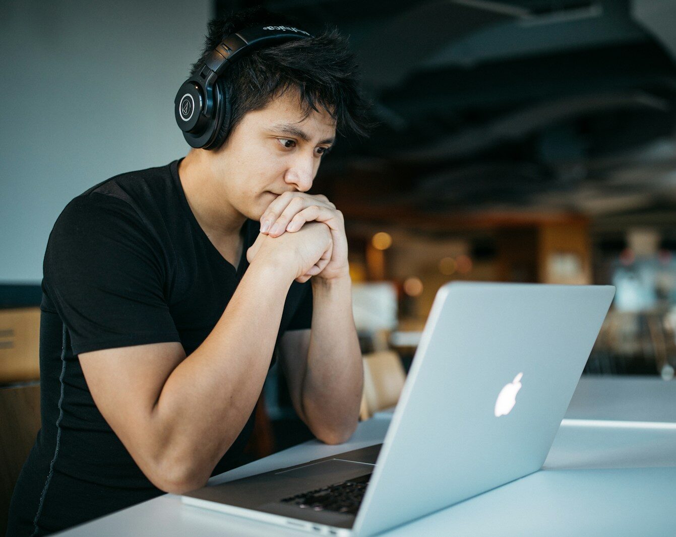 man wearing headphones while sitting on chair in front of MacBook